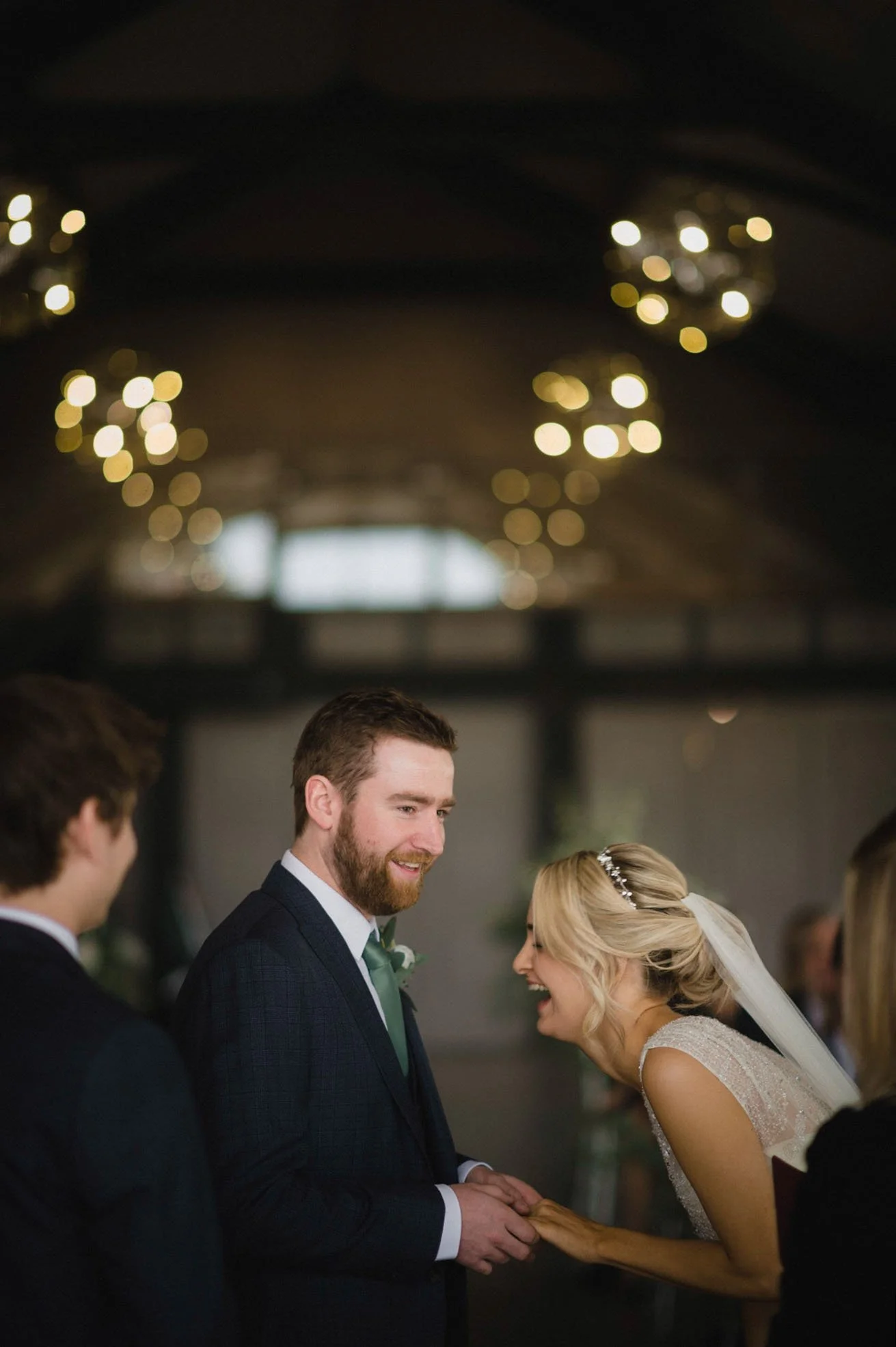 Bride and groom holding hands during their wedding ceremony, smiling and looking at each other in a decorated indoor venue.