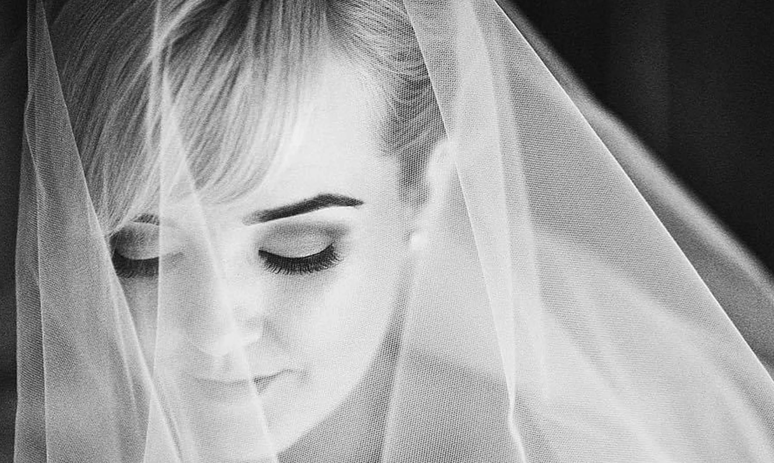 Close-up of a bride with eyes closed, wearing a veil, in black and white.