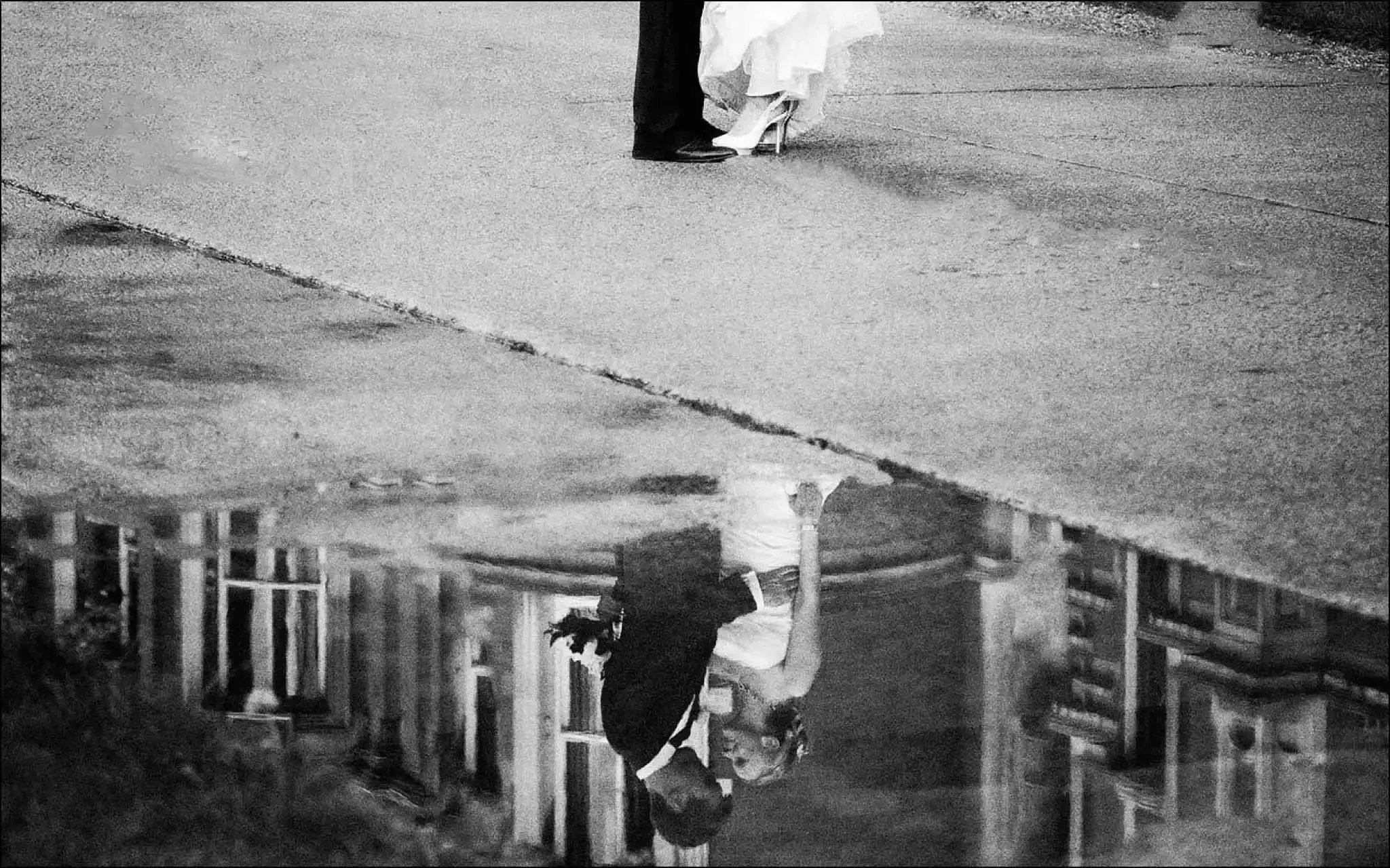 A bride and groom share a kiss, their reflection gleaming in a puddle—captured by a Yorkshire wedding photographer.