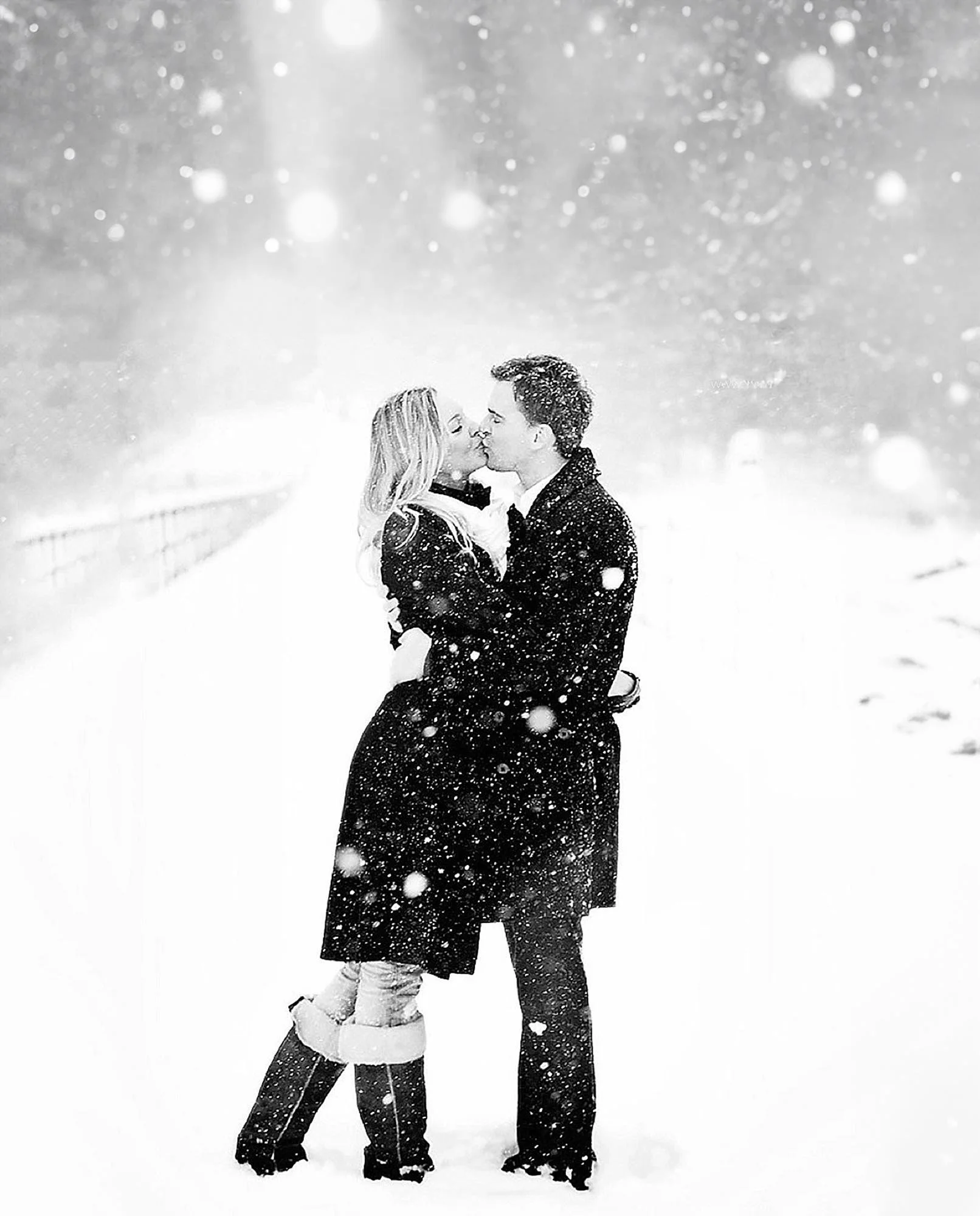 snowy day romatic black and white photo of a couple kissingin a snow fall