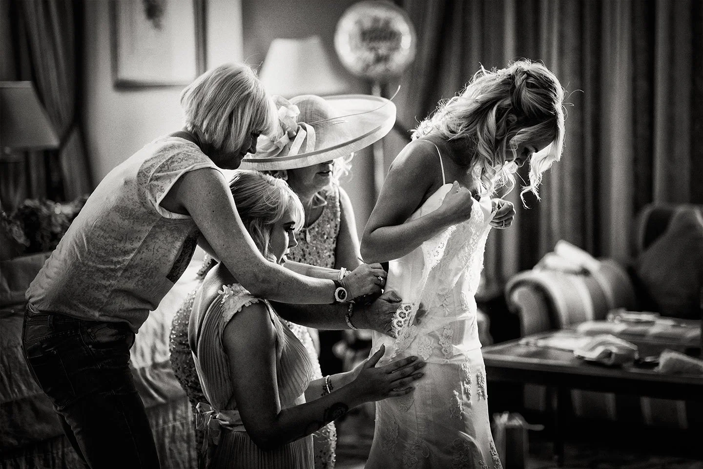 BRIDE BEING HELPED BY HER FAMILY PUTTING HER WEDDING DRESS ON