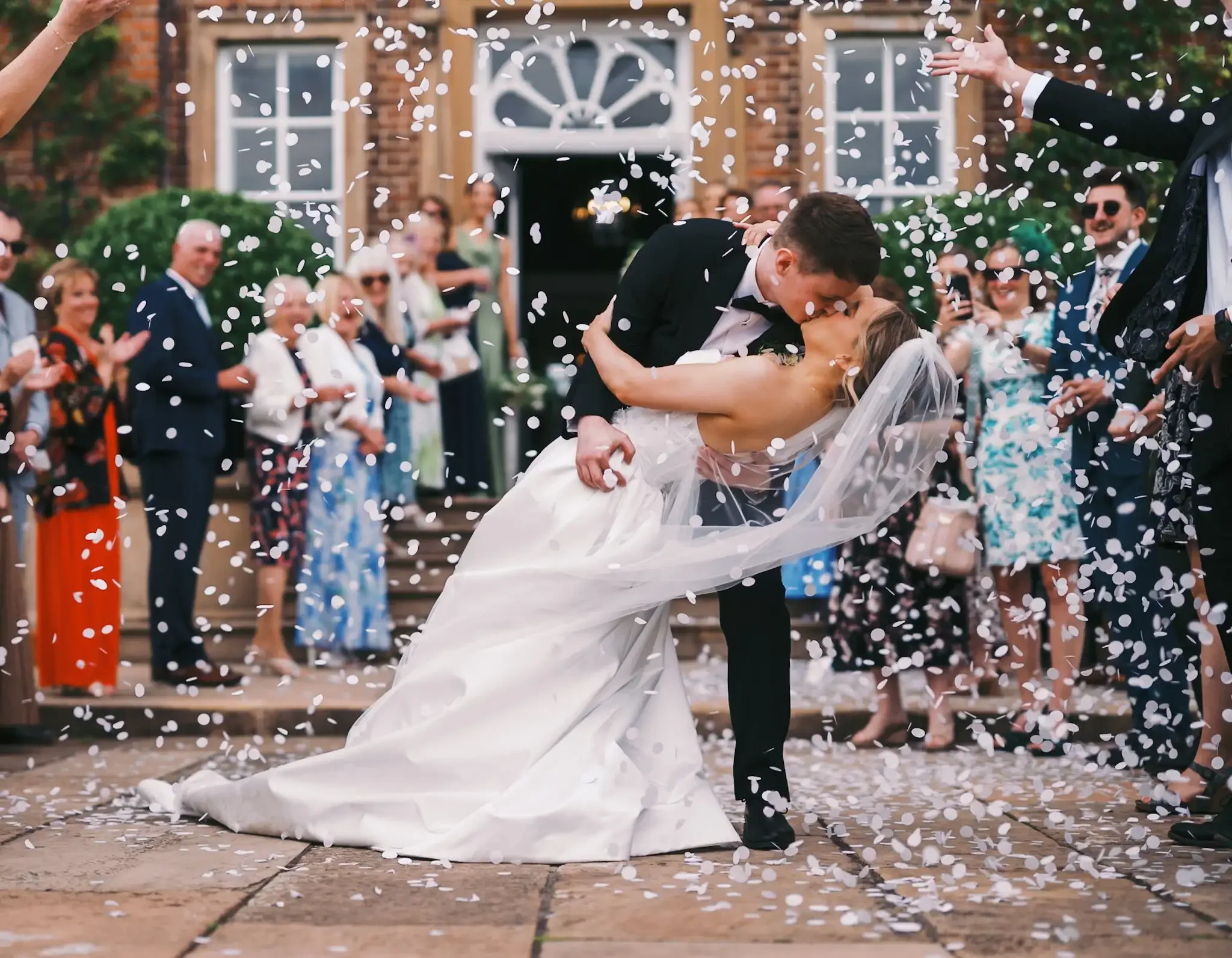 bride and groom doing a 'dip' whilst guests throw confeeti on them. photo taken by norwood wedding photographer in front of the main house