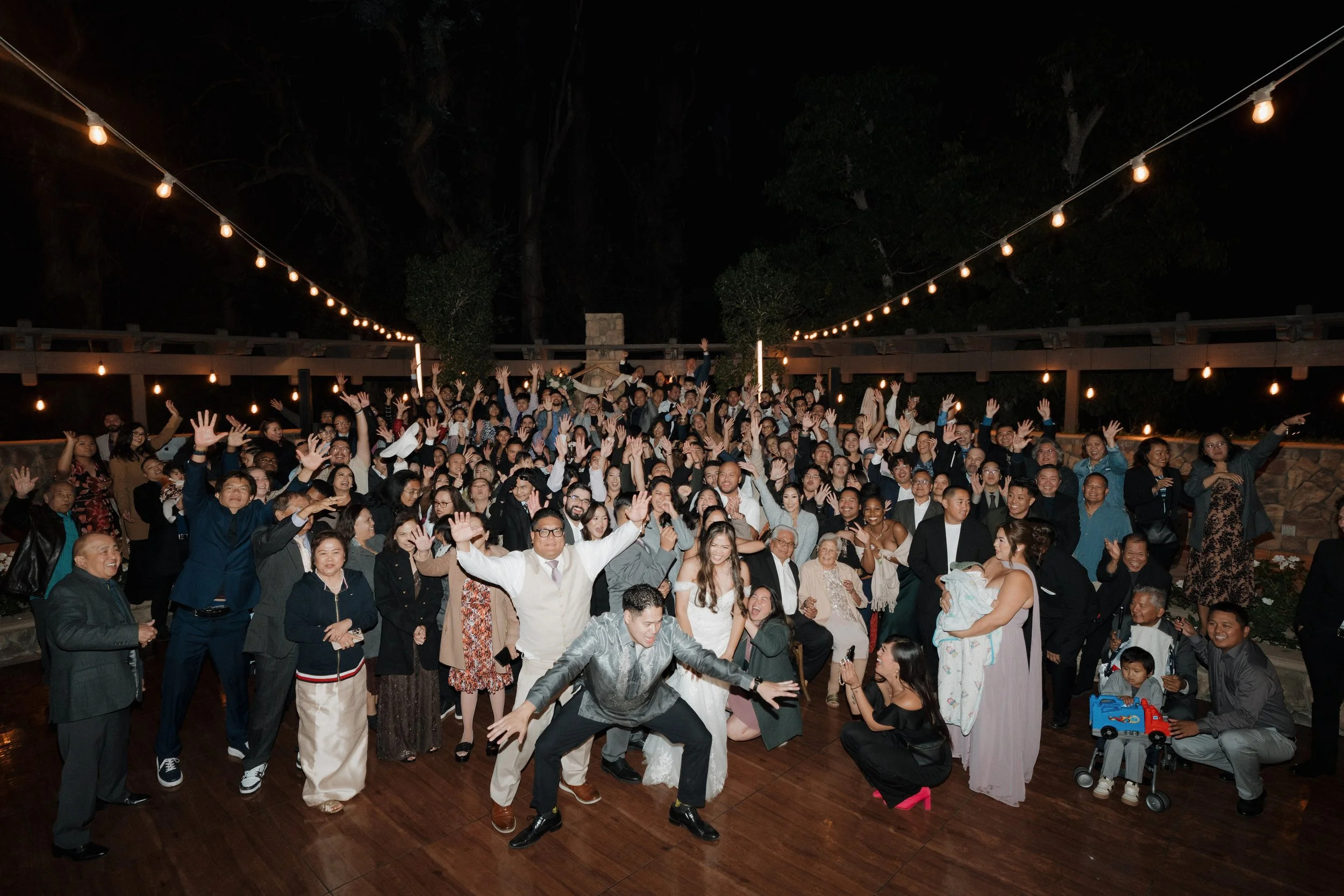 Large group of people gathered outdoors at night, celebrating and posing for a photo under string lights.