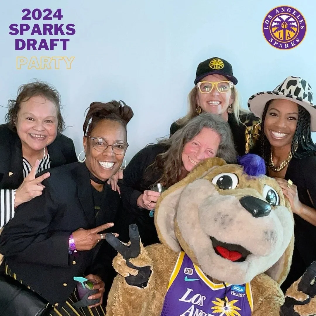 Group of women celebrating the Los Angeles Sparks 2024 draft party with a mascot holding a basketball, wearing sports jerseys and accessories.