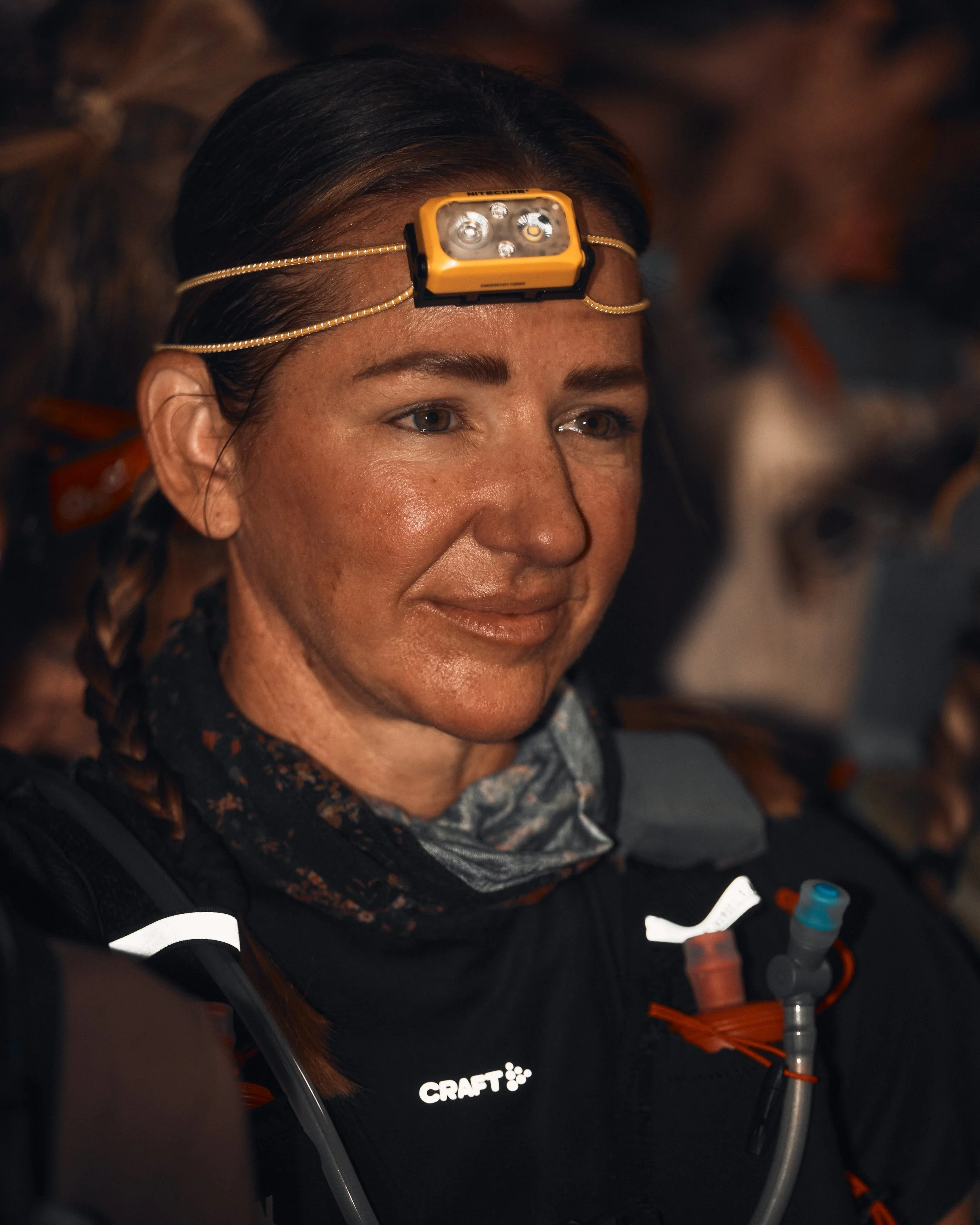 Close-up of a woman wearing a headlamp and hiking gear, with the brand 'CRAFT' visible on her shirt.