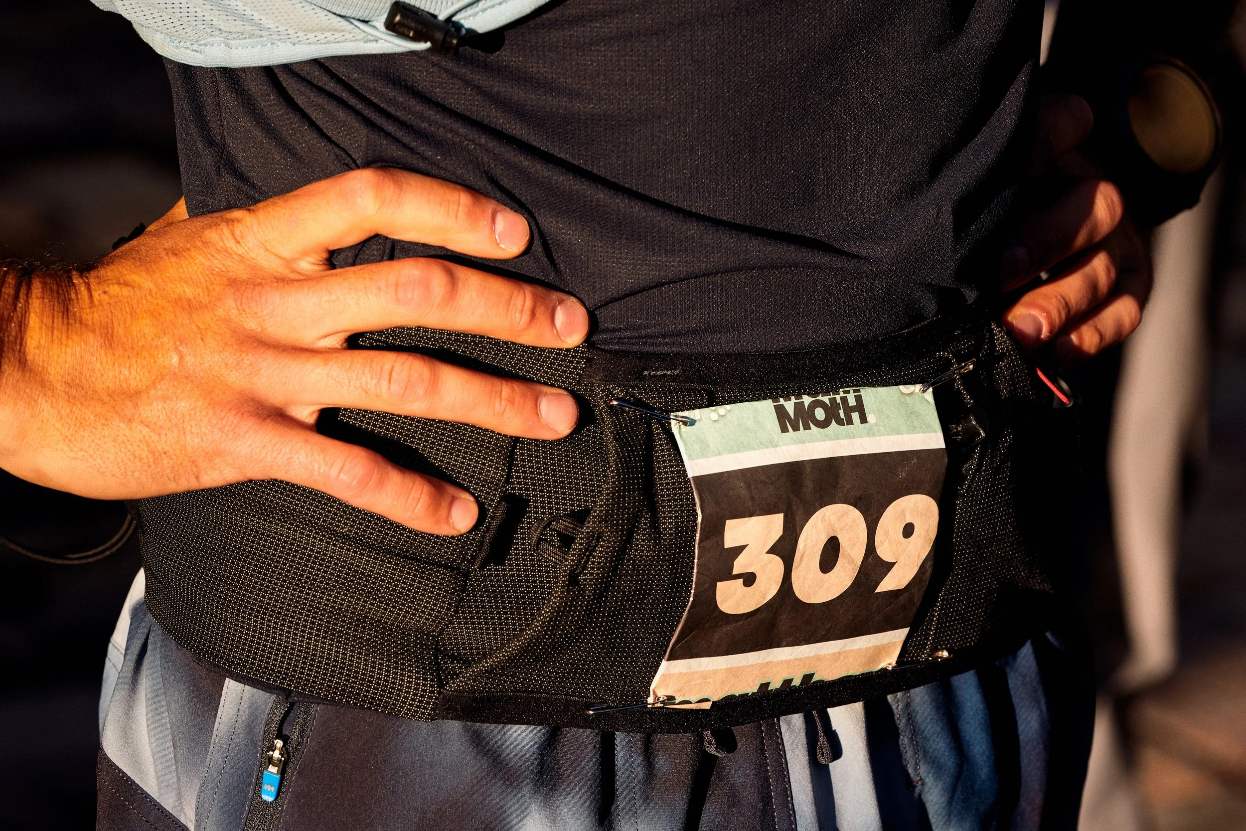 Close-up of a person wearing a black shirt and a bib number with the number 308, standing with hands on hips. 