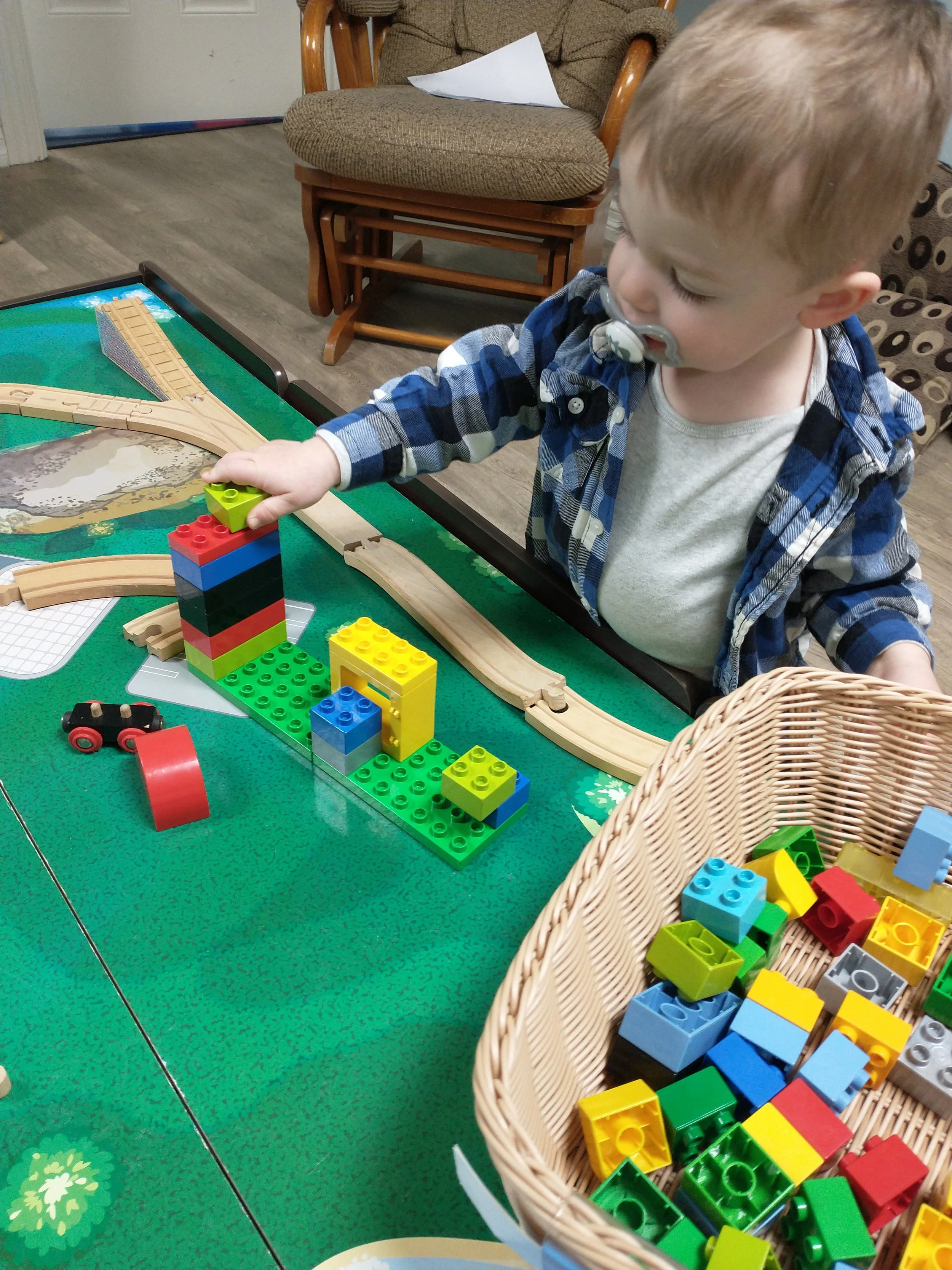 Child playing with LEGO DUPLO blocks on a table next to a wicker basket filled with blocks.
