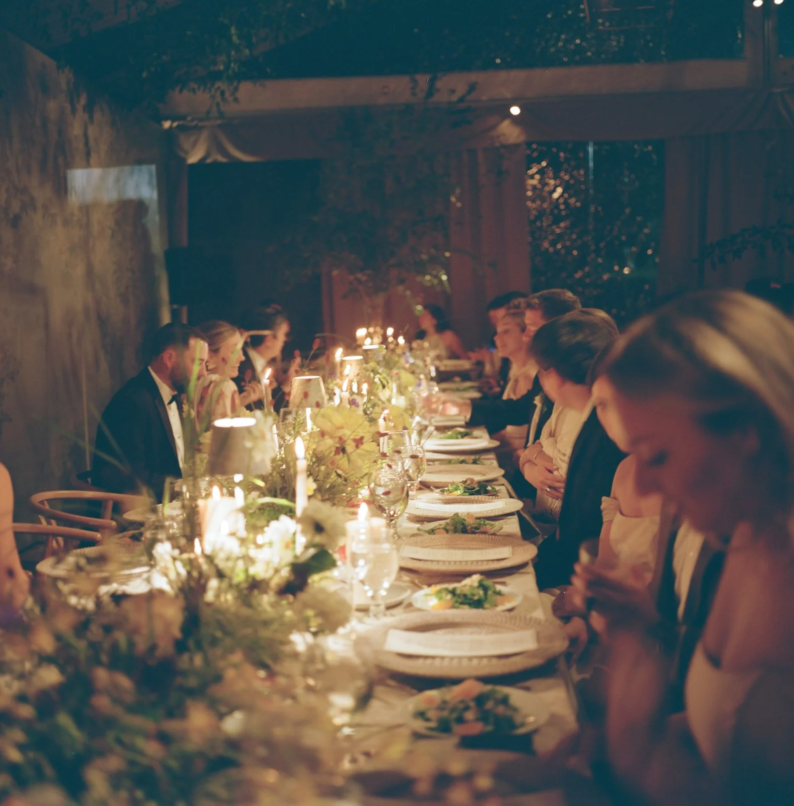 People dining at a long, elegant table decorated with flowers and candles in a warmly lit setting