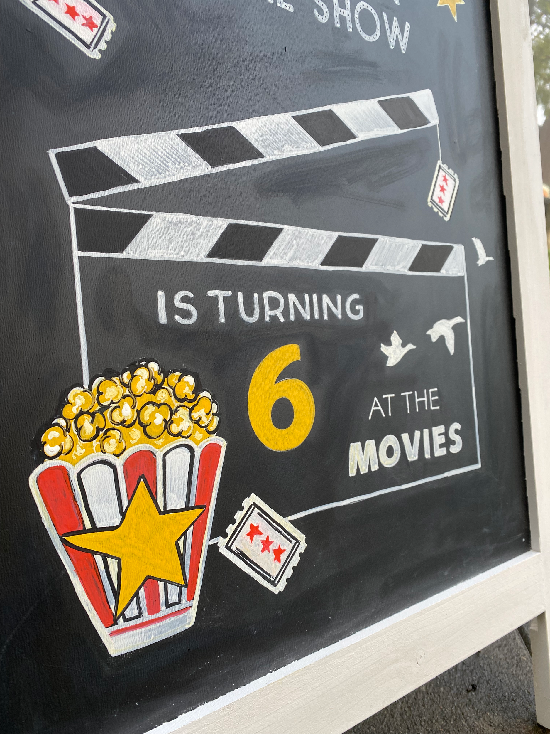 A closeup of a Movie themed birthday party chalkboard with hand drawn popcorn and movie clapperboard with a yellow 6.