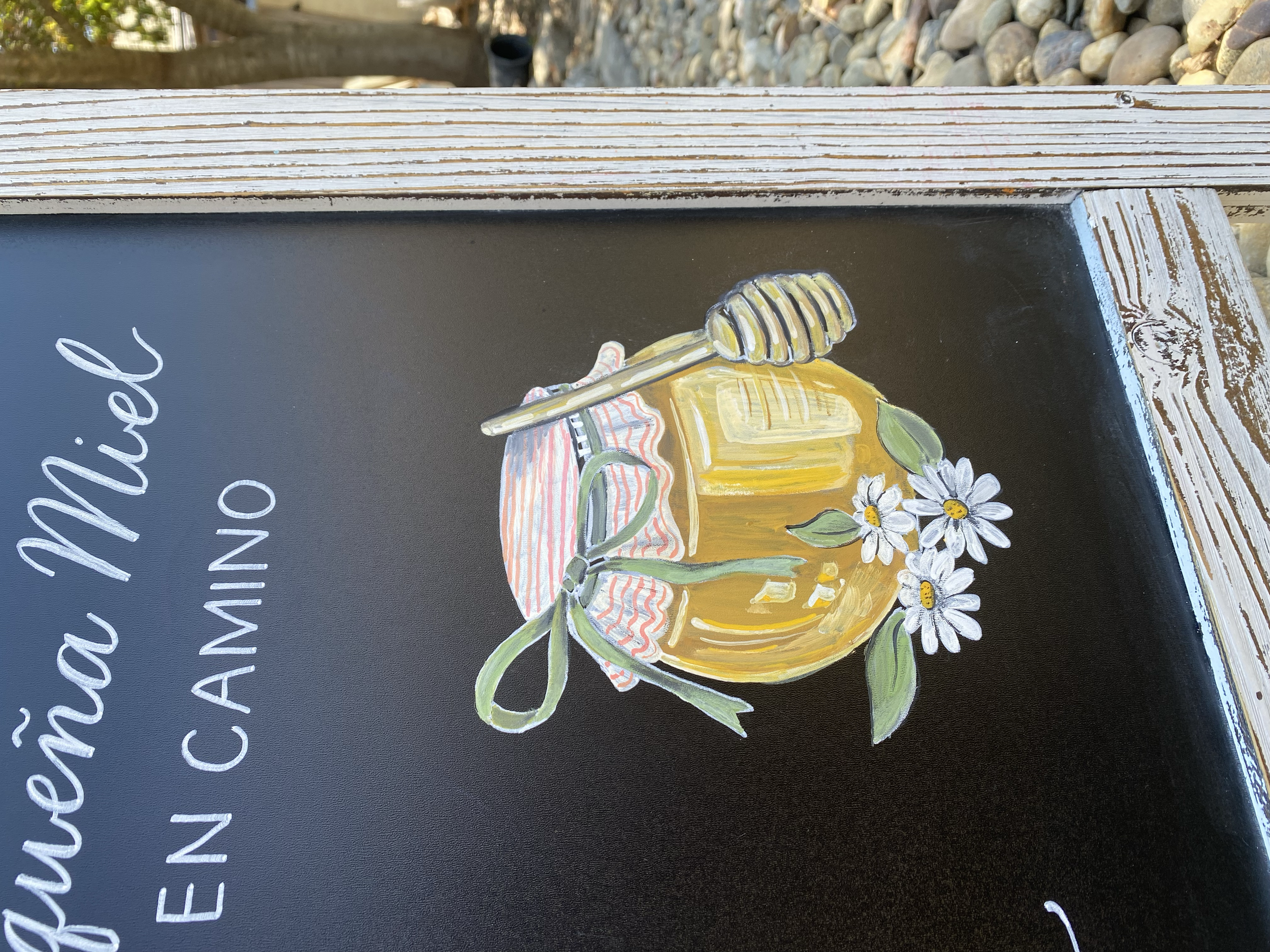 Up close image of a chalkboard with hand illustrated golden honey pot with a cluster of white daisies.