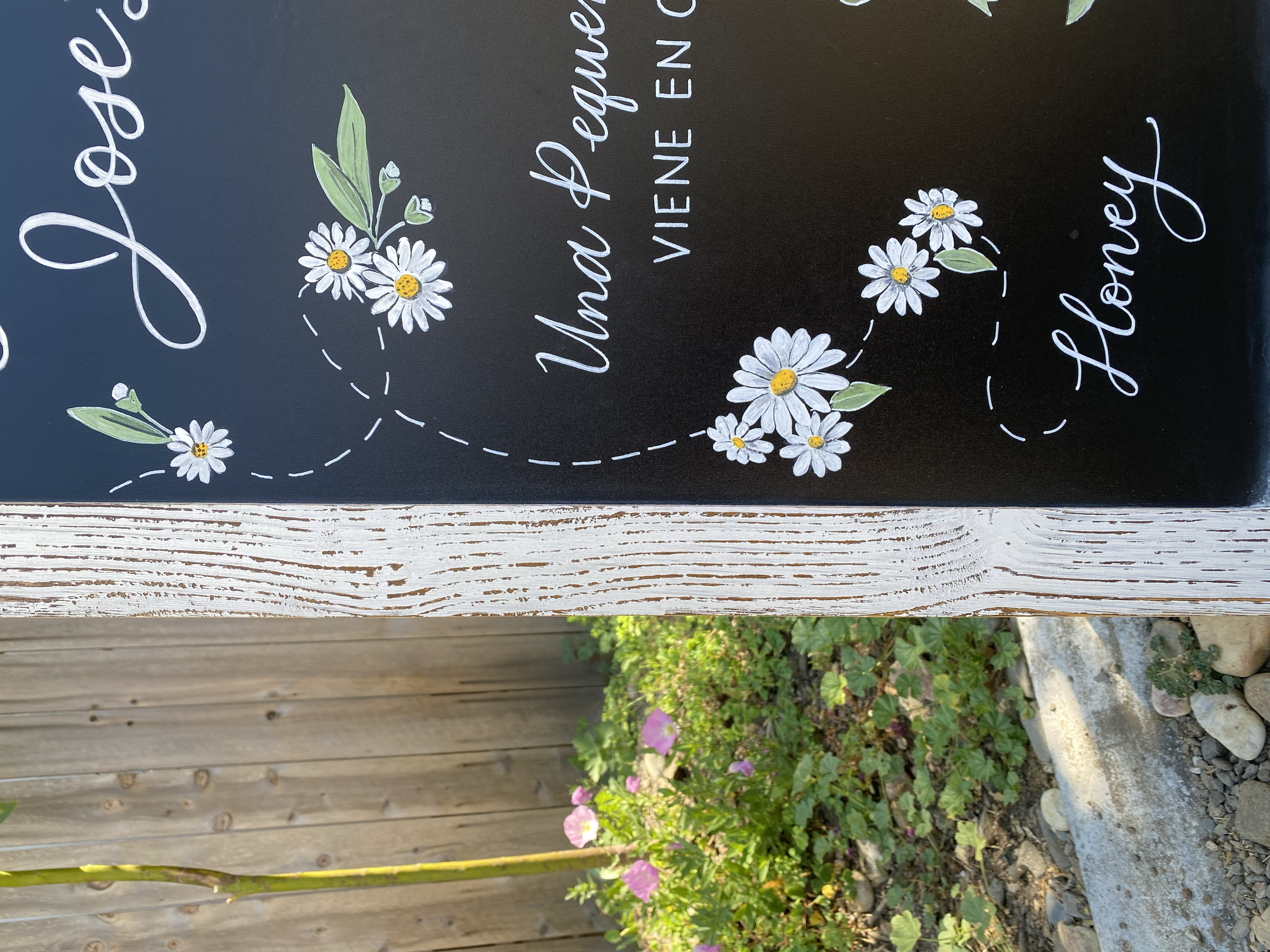 Up close shot of a baby shower chalkboard with details of white daisy clusters with green leaves.