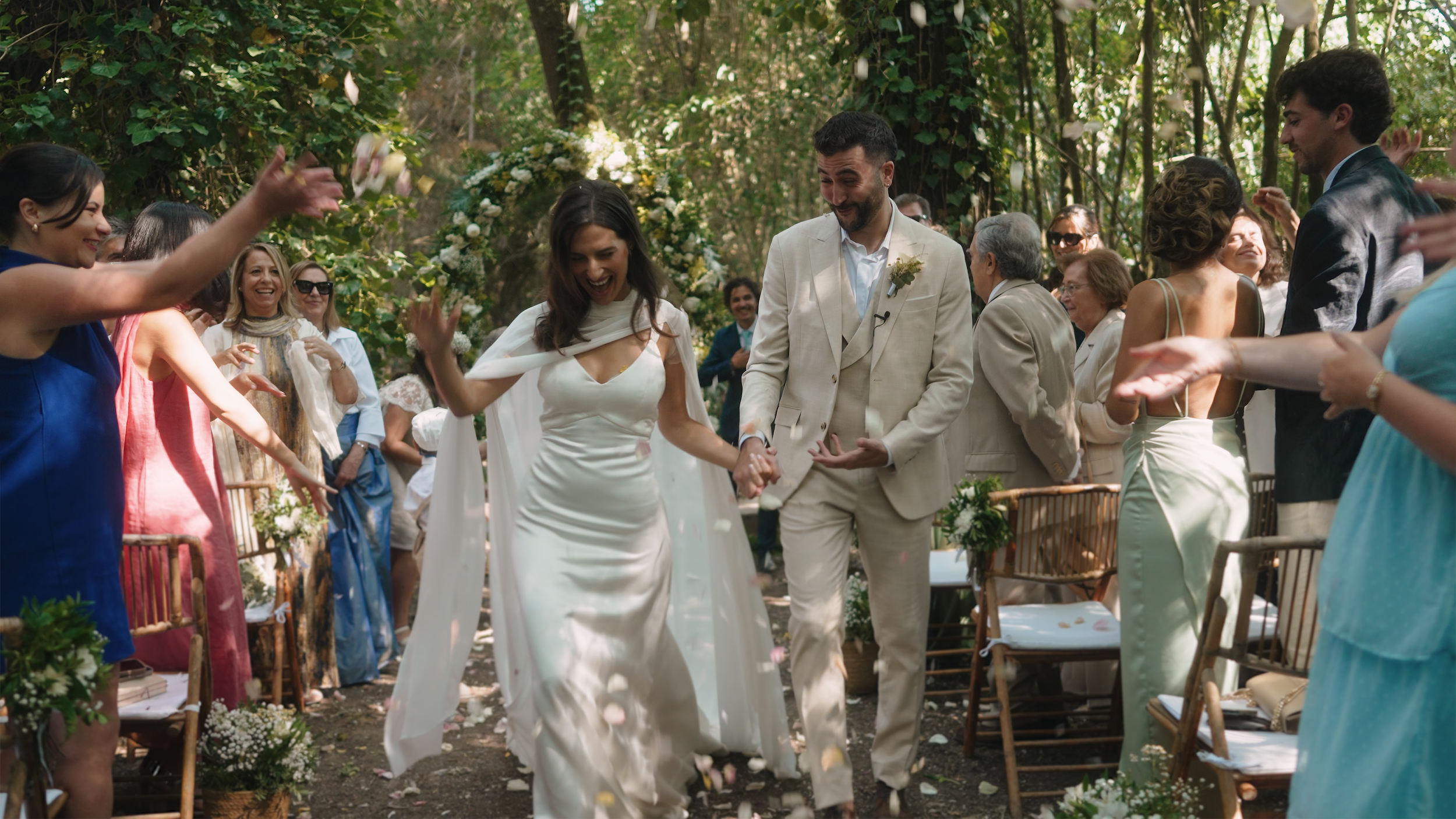 Bride and groom walking hand in hand down the aisle, celebrating at their outdoor wedding ceremony with family and friends throwing flower petals.