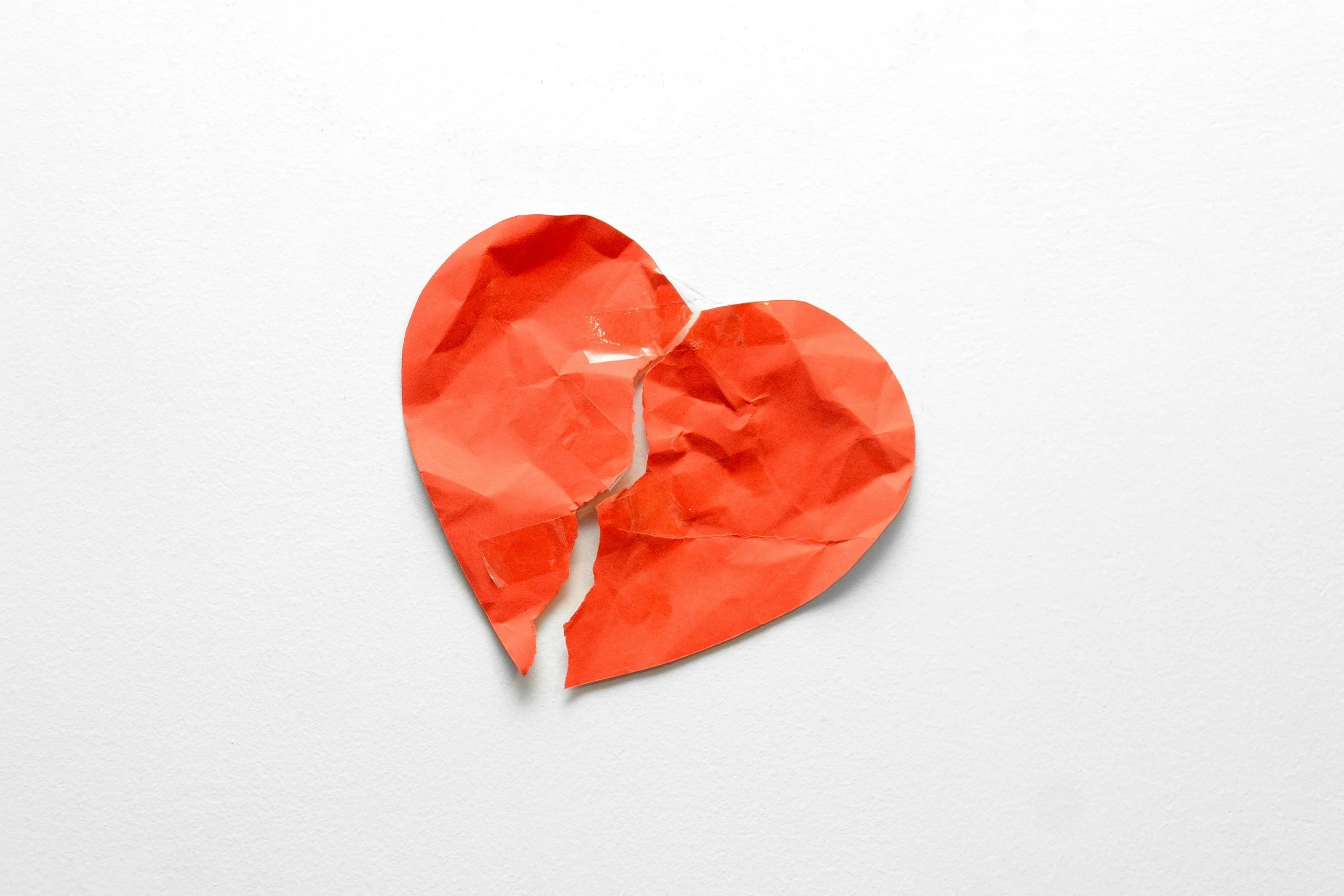 Crumpled red paper shaped like a broken heart on a white surface.