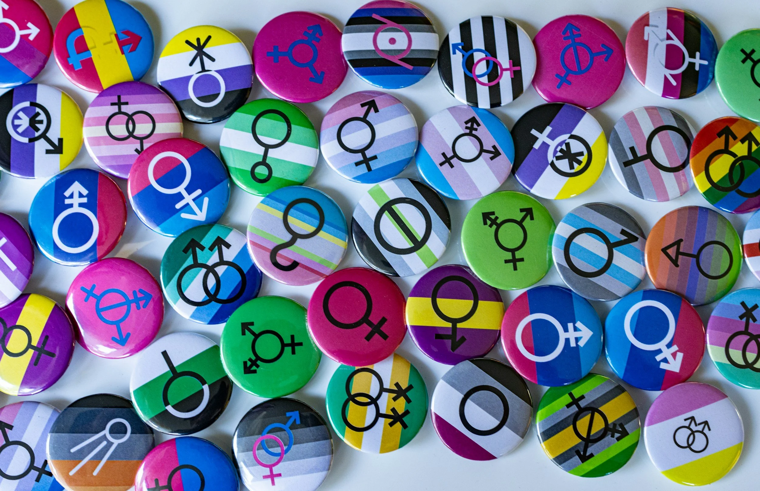 Collection of colorful round pins featuring various gender symbols on a white background.