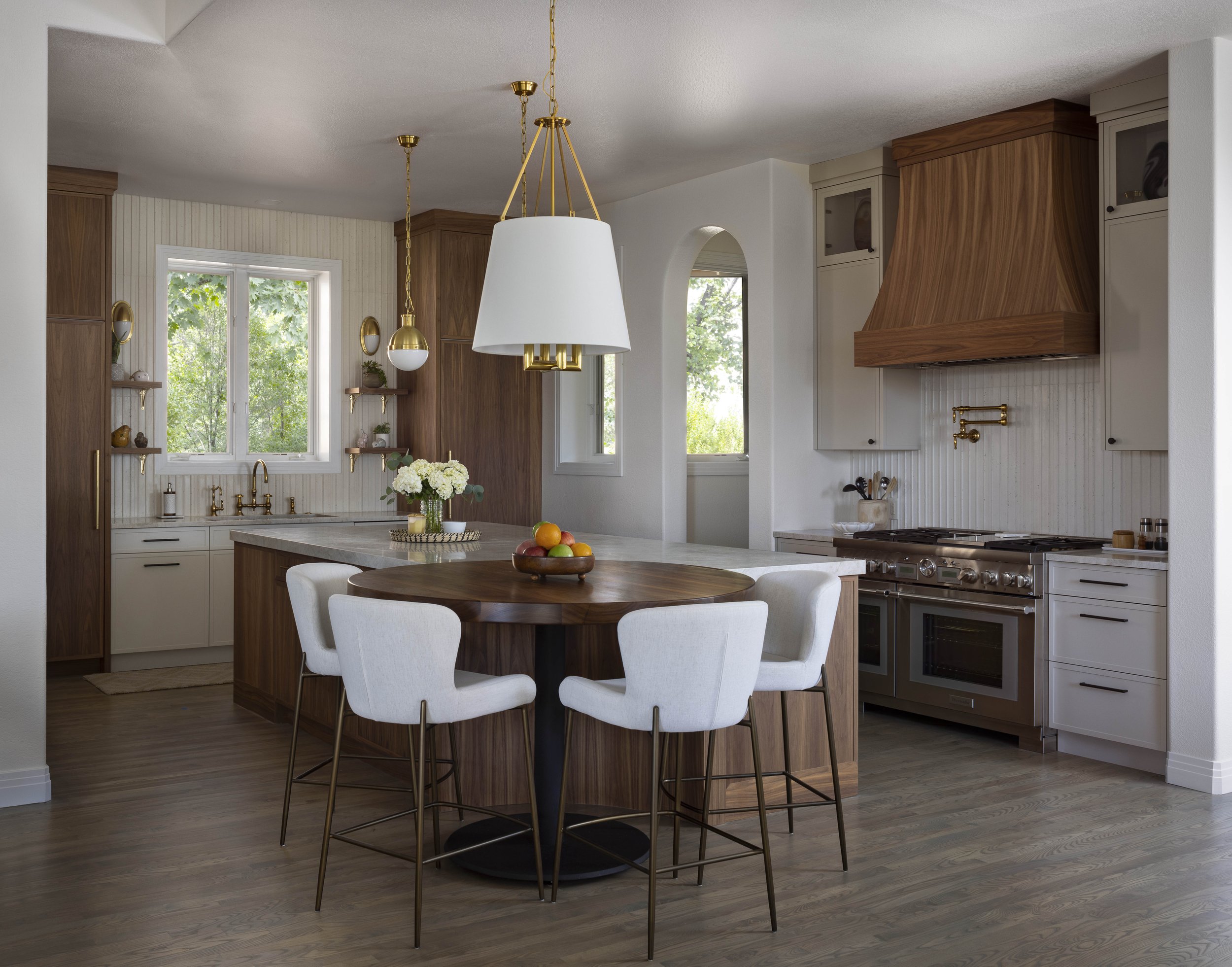 Modern kitchen with painted (sherwin williams accessible beige) and walnut cabinetry, a central island, a round custom made walnut dining table with white chairs, and large windows letting in natural light.