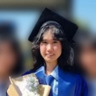 A woman smiling with closed eyes, wearing pearl jewelry, red and gold makeup, and decorative face gems, posing against a red curtain backdrop.