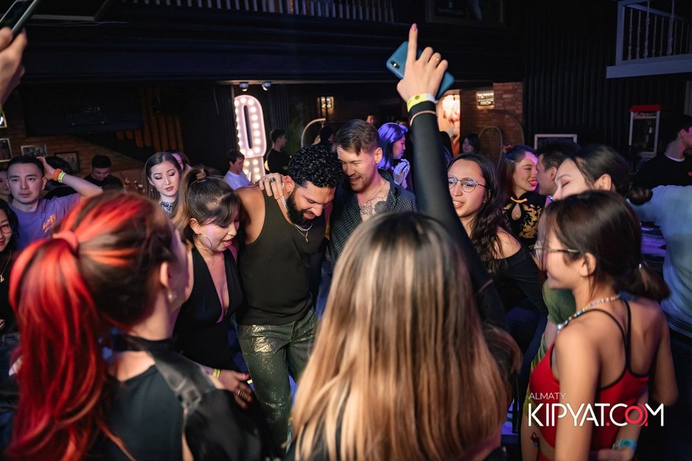Almaty, Kazakhstan — Group of people dancing and enjoying music at a nightclub or party, with some individuals smiling and others raising their hands.