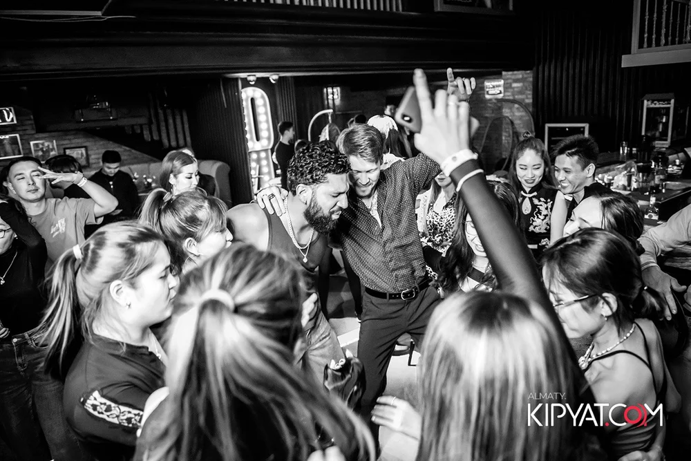 Almaty, Kazakhstan — A group of people dancing and socializing at a party in a bar or club, with some holding drinks and enjoying the music.