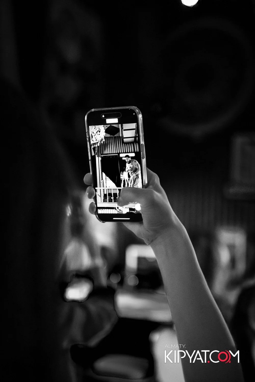 Almaty, Kazakhstan — Person taking a photo with a smartphone of a performer on stage, captured in black and white.