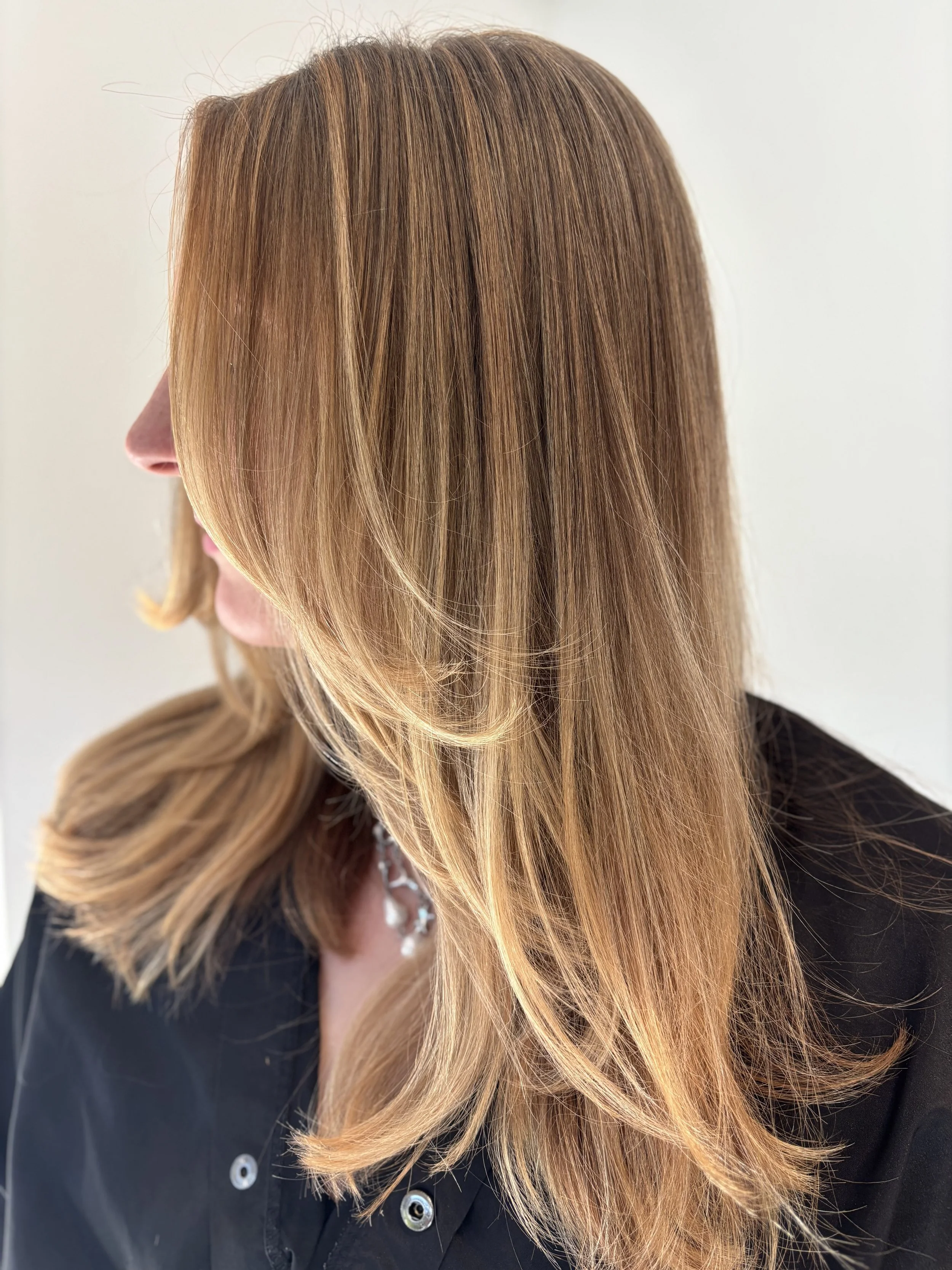 Close-up of a classic style woman with a butterfly haircut and caramel-colored hair, wearing a dark shirt, against a light background.