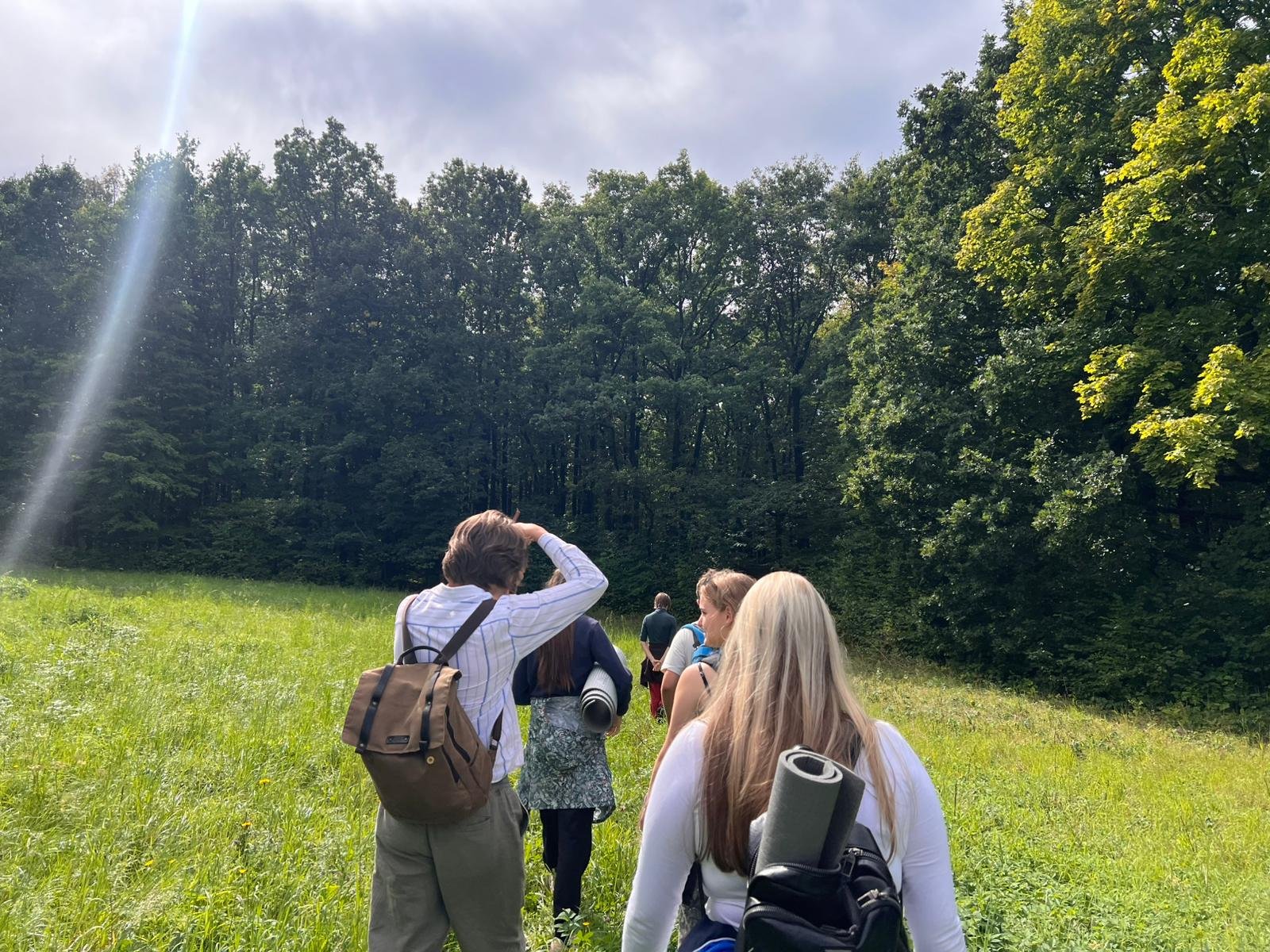 Grupa młodzieży z plecakami idzie przez łąkę w stronę lasu