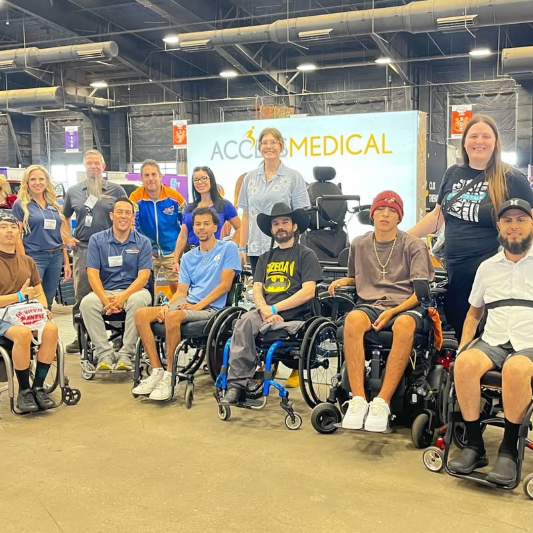 A diverse group of people, including individuals in wheelchairs, posing together at an event with a large sign in the background that reads 'ACCESS MEDICAL'.