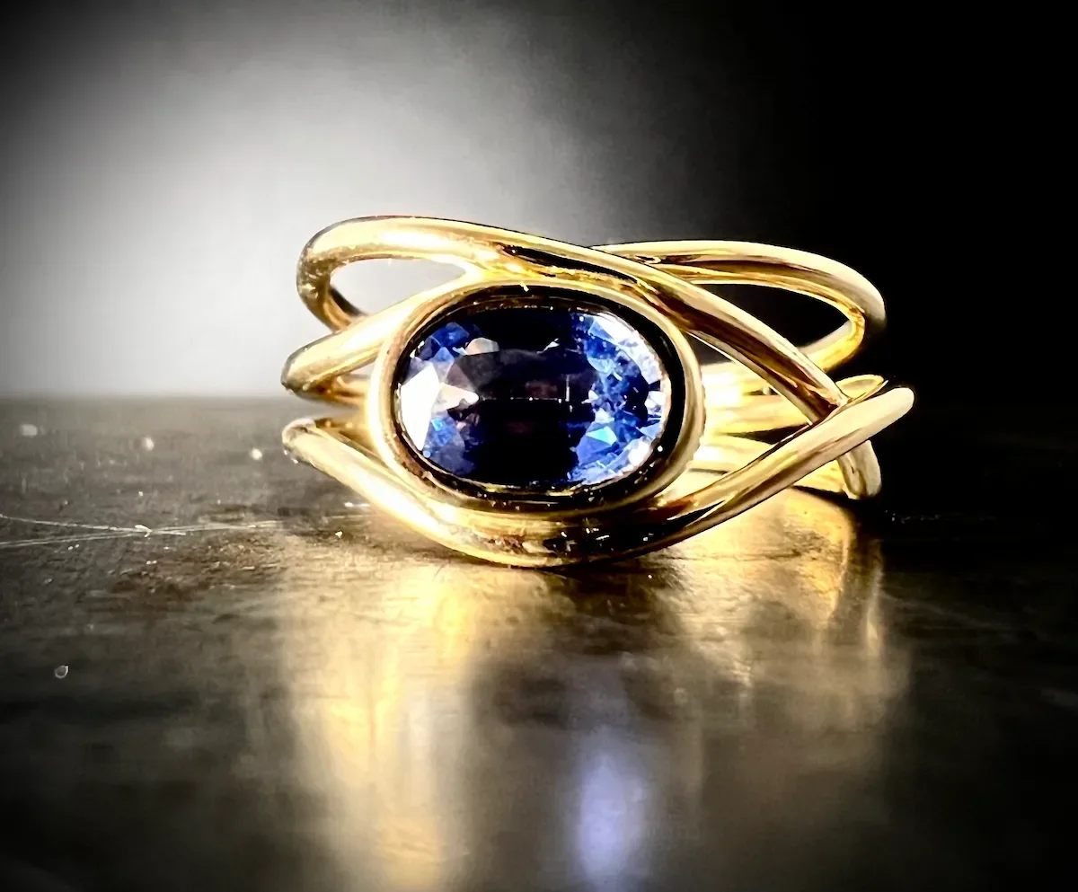 Organischer Ring aus Gelbgold mit ovalem blauen Saphir in Zargenfassung, handgefertigt in München.