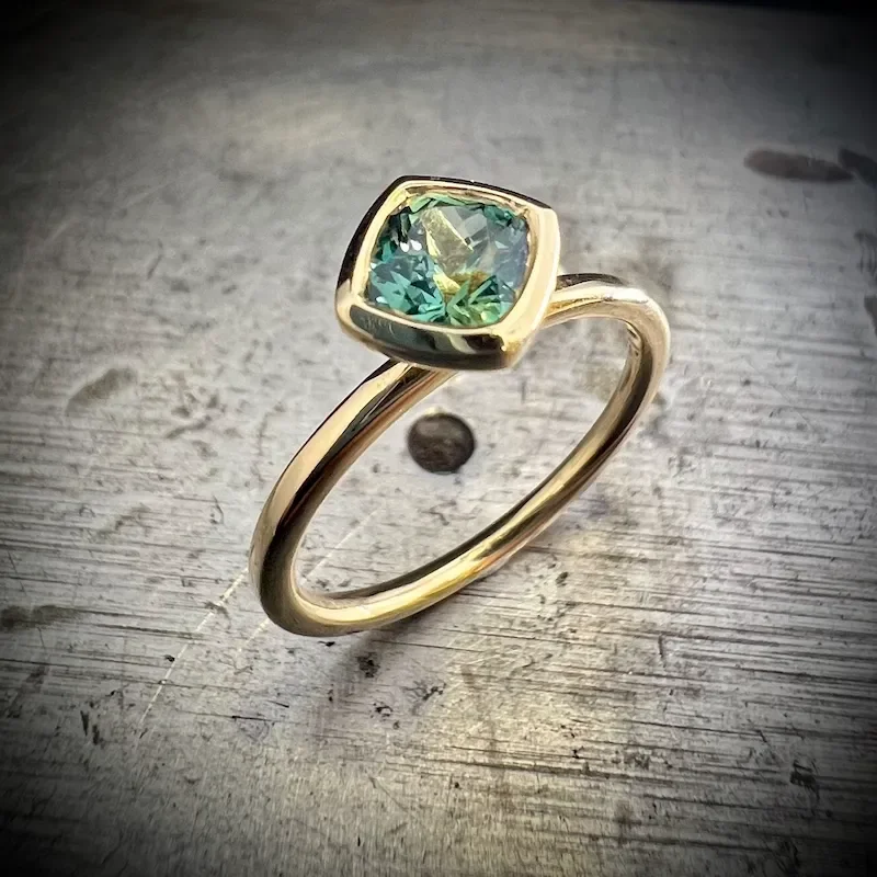 Moderner Verlobungsring aus recyceltem Gold mit einem quadratisch geschliffenen Saphir in Grün-Gelb-Nuancen, gefasst in einer markanten Zarge