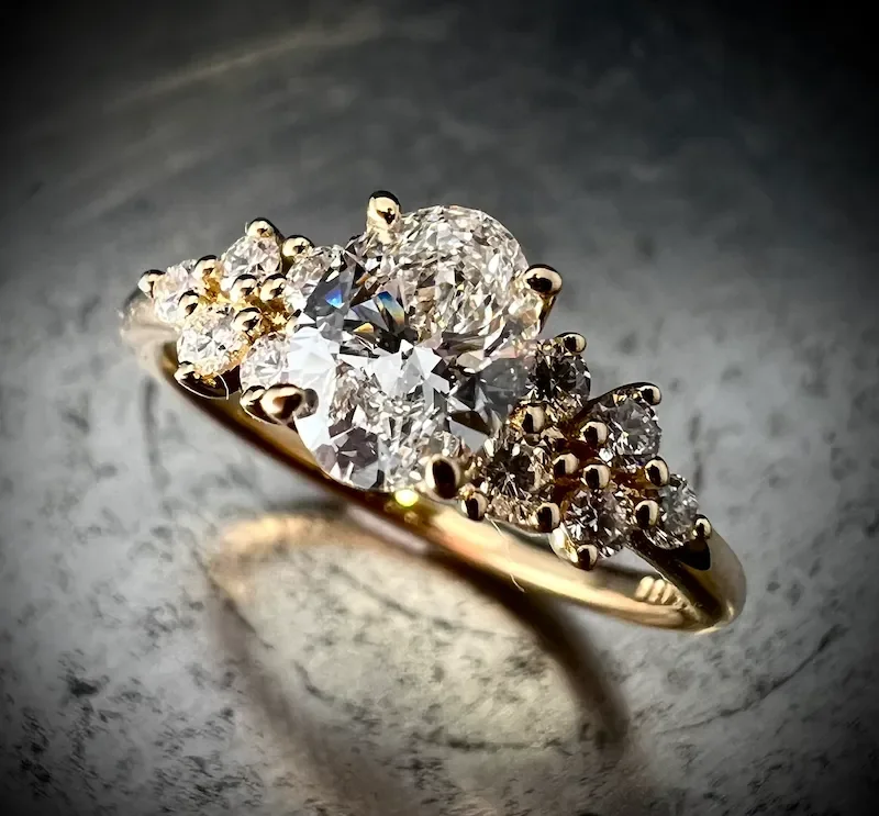 Verlobungsring aus Gelbgold mit ovalem Diamanten und seitlichem Cluster-Besatz, Isarschmiede München.