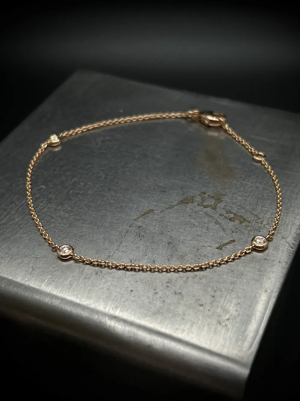 Goldene Armkette mit kleinen Diamanten, liegend auf einer metallischen Oberfläche.