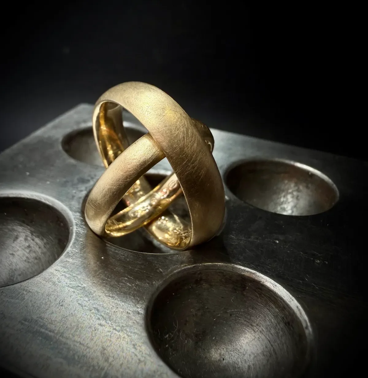 Zwei goldene Eheringe auf einem Metall-Ei, gegen einen schwarzen Hintergrund.