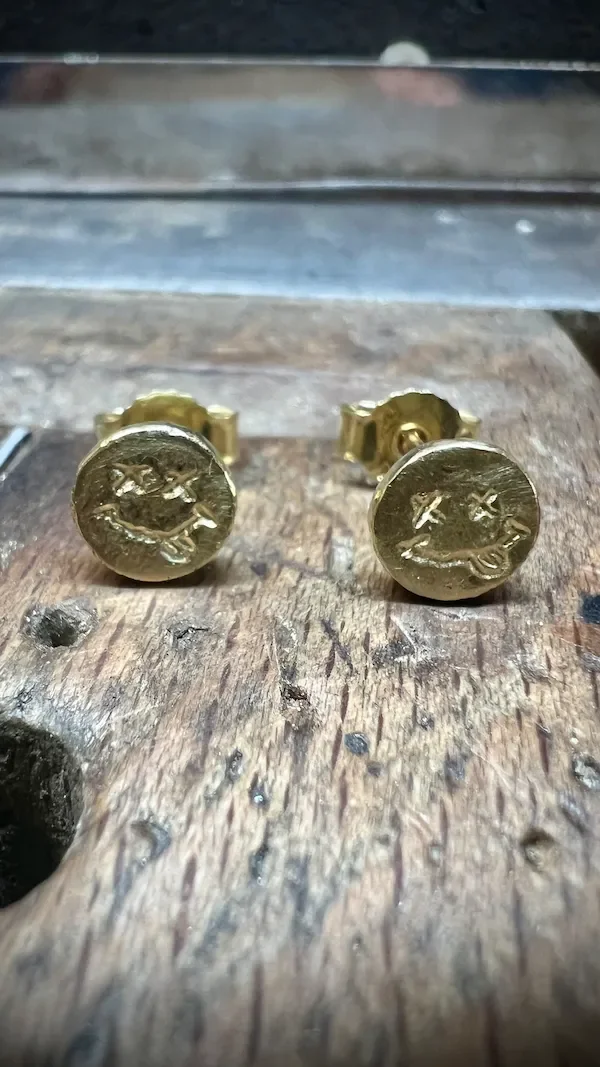 Ohrstecker aus Gold mit einem gravierten Smiley, auf einem Goldschmiede Feilnagel.