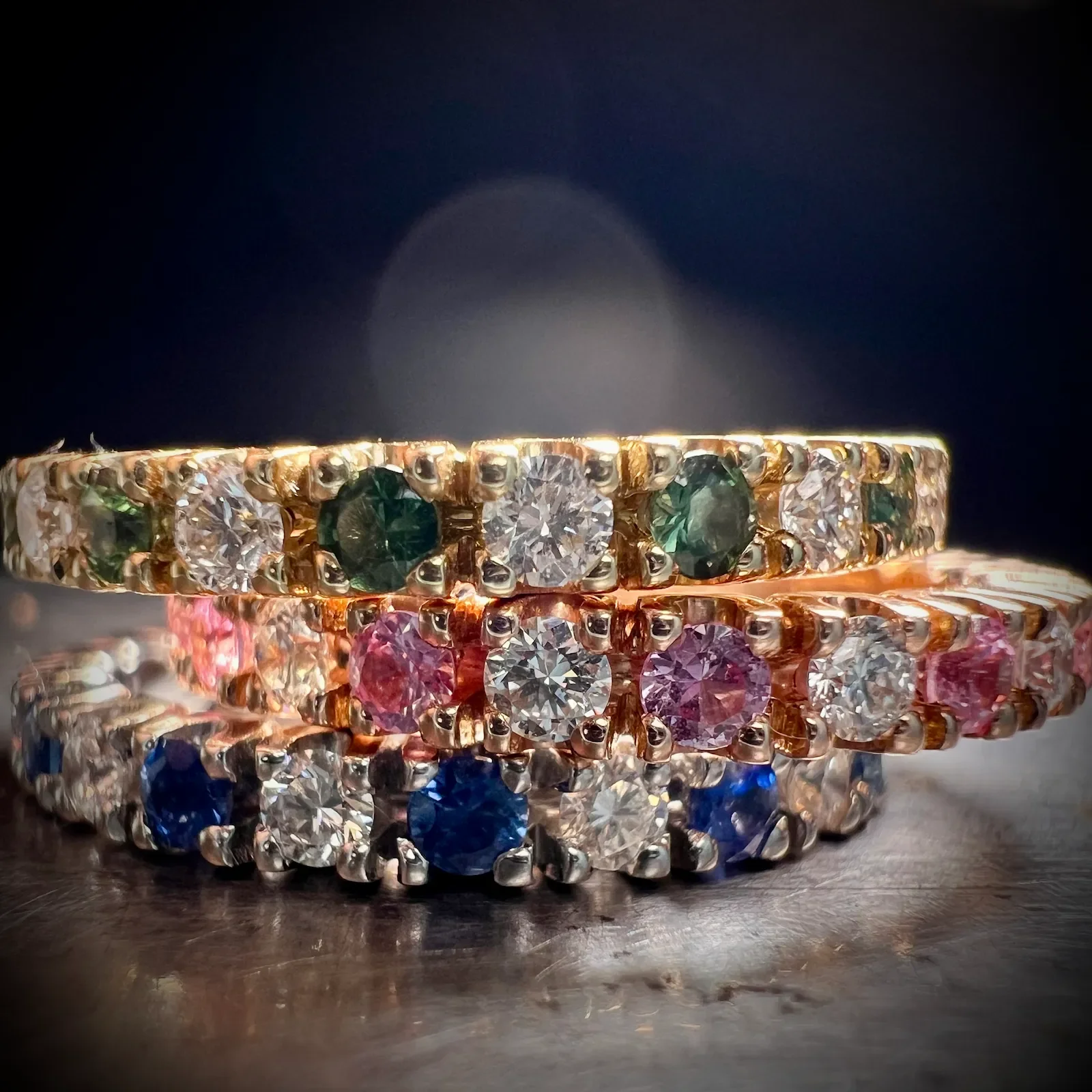 Drei Memoire-Ringe mit weißen Diamanten und Saphiren in blau, grün und rosa, aufgenommen im Nahaufnahme-Modus.