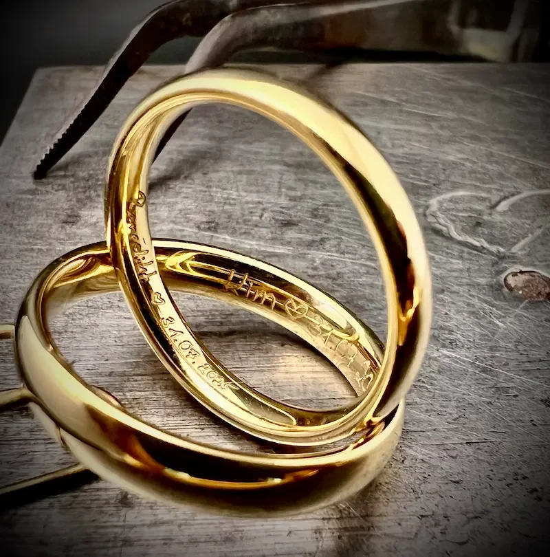 Drei goldene Ringe liegen auf einer holzverkleideten Oberfläche, umgeben von Werkzeugen, vermutlich für Schmuckherstellung.