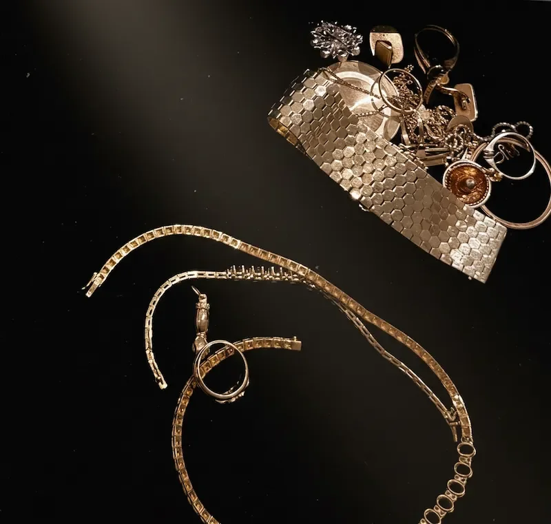 Verschiedene goldene Schmuckstücke, darunter Ketten und Ringe, liegen auf einem schwarzen Hintergrund und werden vorbereitet zu recyceln.