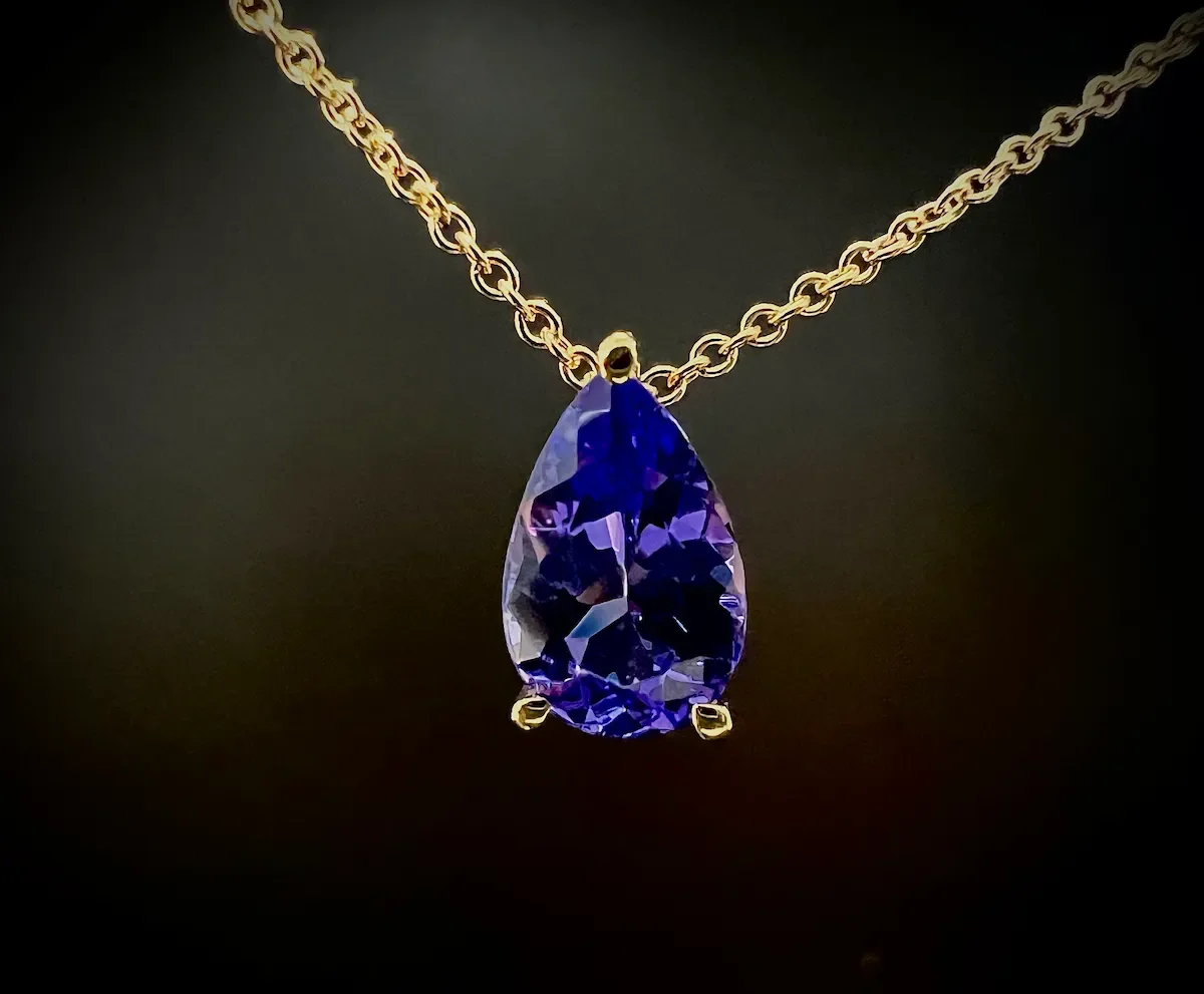 Goldene Kette mit blauviolettem Tansanit an einem schwarzen Hintergrund