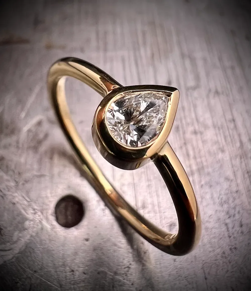 Minimalistischer Verlobungsring aus Gelbgold mit Diamant im Tropfenschliff in Zargenfassung, Isarschmiede München.