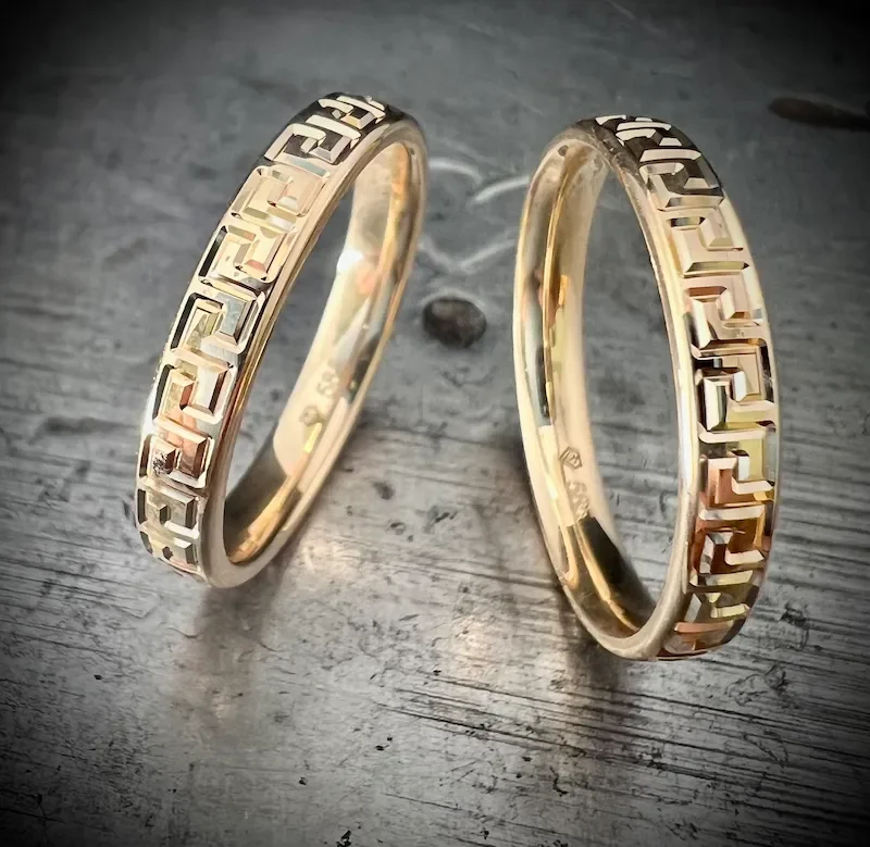 Zwei goldene Eheringe mit einem geometrischen Muster auf einer Holzoberfläche.