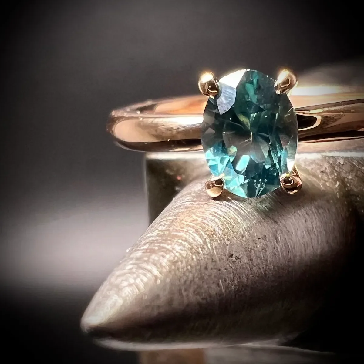 Solitär-Verlobungsring aus Gelbgold mit ovalem Petrol-Saphir auf Werkzeug, handgefertigt in München.