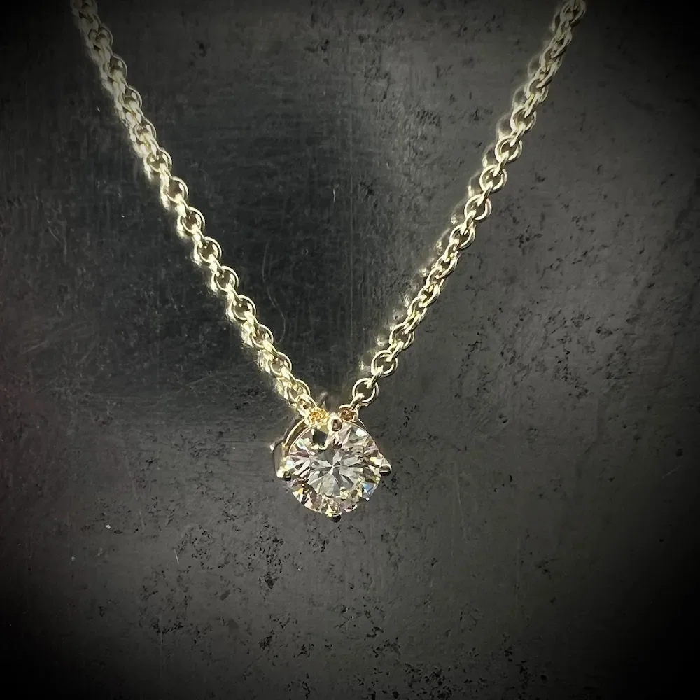 Silberne Halskette mit einem großen, runden Diamanten an einem dunklen Hintergrund.