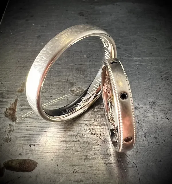 Zwei Silberringe liegen auf einer dunklen Metalloberfläche