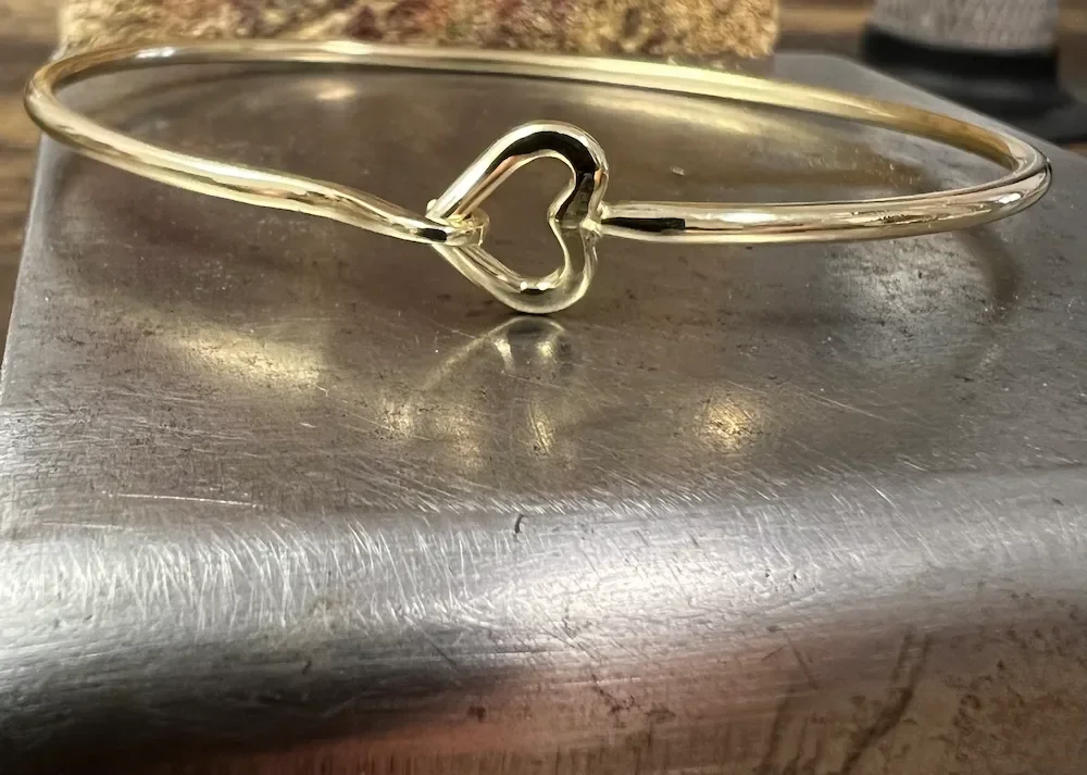 Goldener Armreif mit Herzverschluss auf einer metallischen Oberfläche.