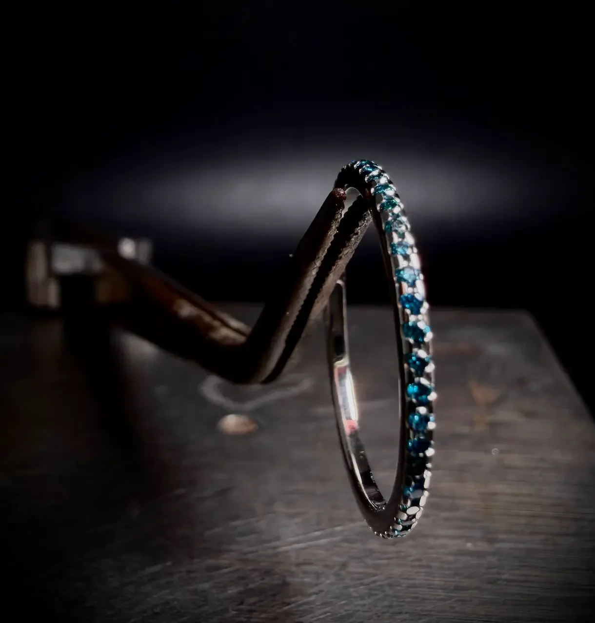 Ein silberner Armband mit blauen Steinen, das an einem alten, rostigen Schraubstock hängt, vor schwarzem Hintergrund.