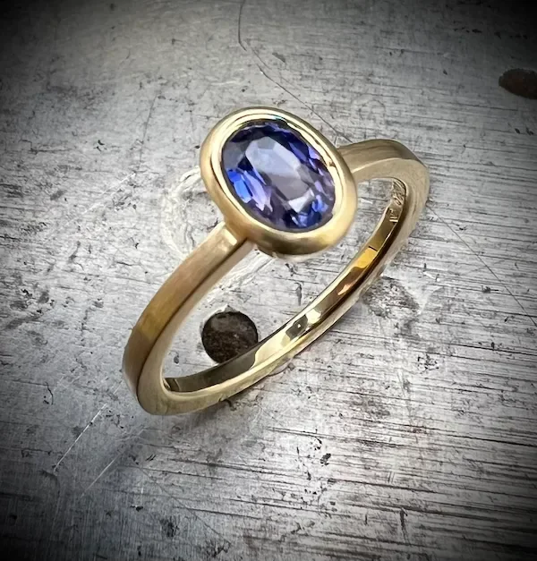 Goldener Ring mit einem ovalen blauen Saphir in einer Zargenfassung  