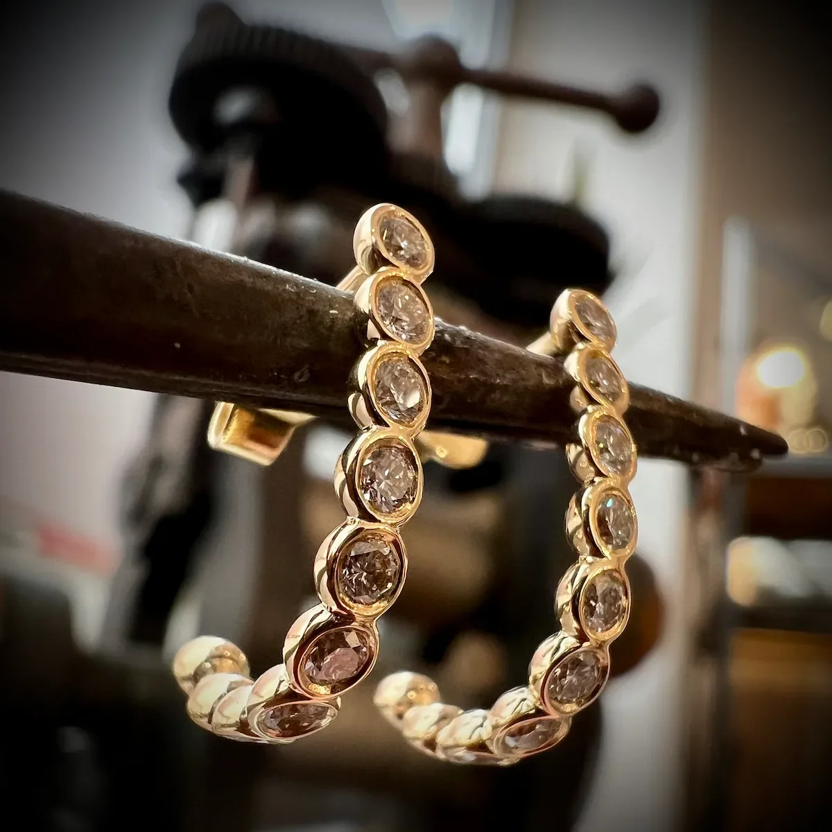 Goldene Ohrringe mit diamantenen Steinen, hängend an einer rostigen Metallstange, im Hintergrund ein Spielzeugmotorrad.