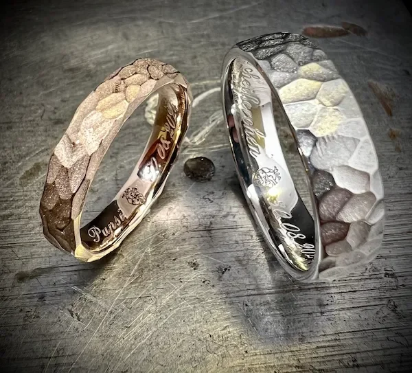 Zwei Ringe mit Hammermuster-Designs auf einer metallischen Oberfläche