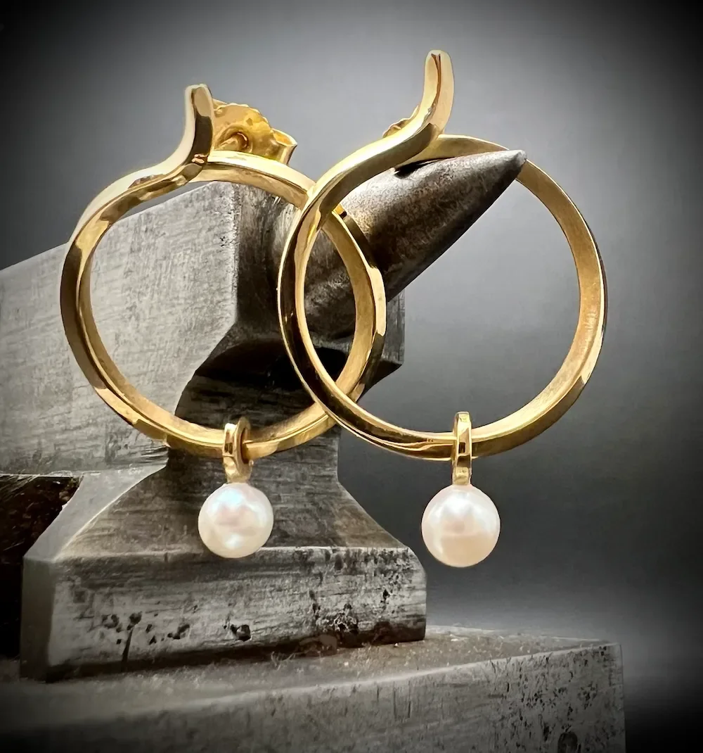 Zwei goldene Ohrringe mit weißen Perlen, display auf einem grauen Amboss.