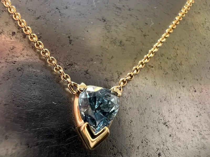 Goldene Halskette mit einem Herzförmigen blauen fairen Saphir als Anhänger auf einer dunklen Oberfläche