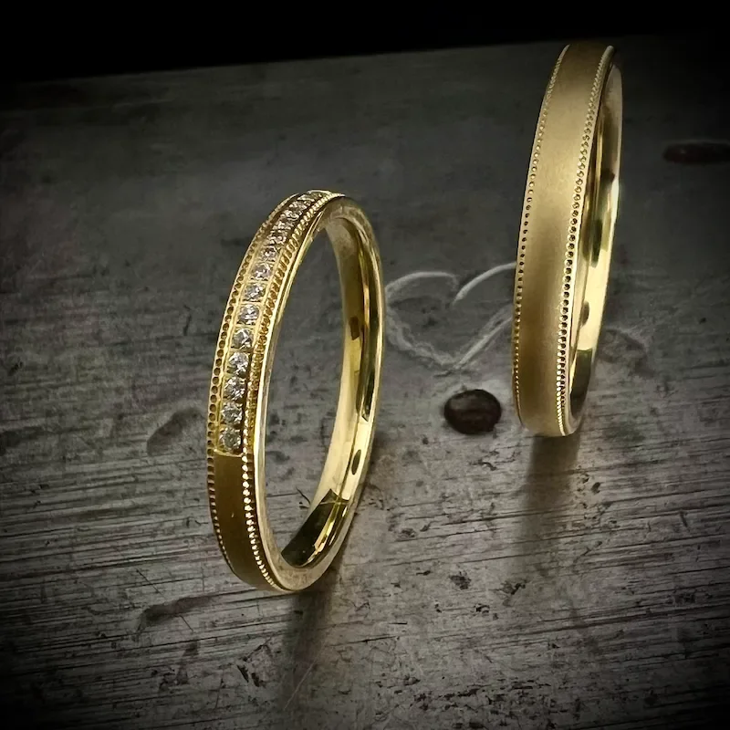 Zwei goldene Eheringe auf einem Holztisch, einer mit Diamanten besetzt.