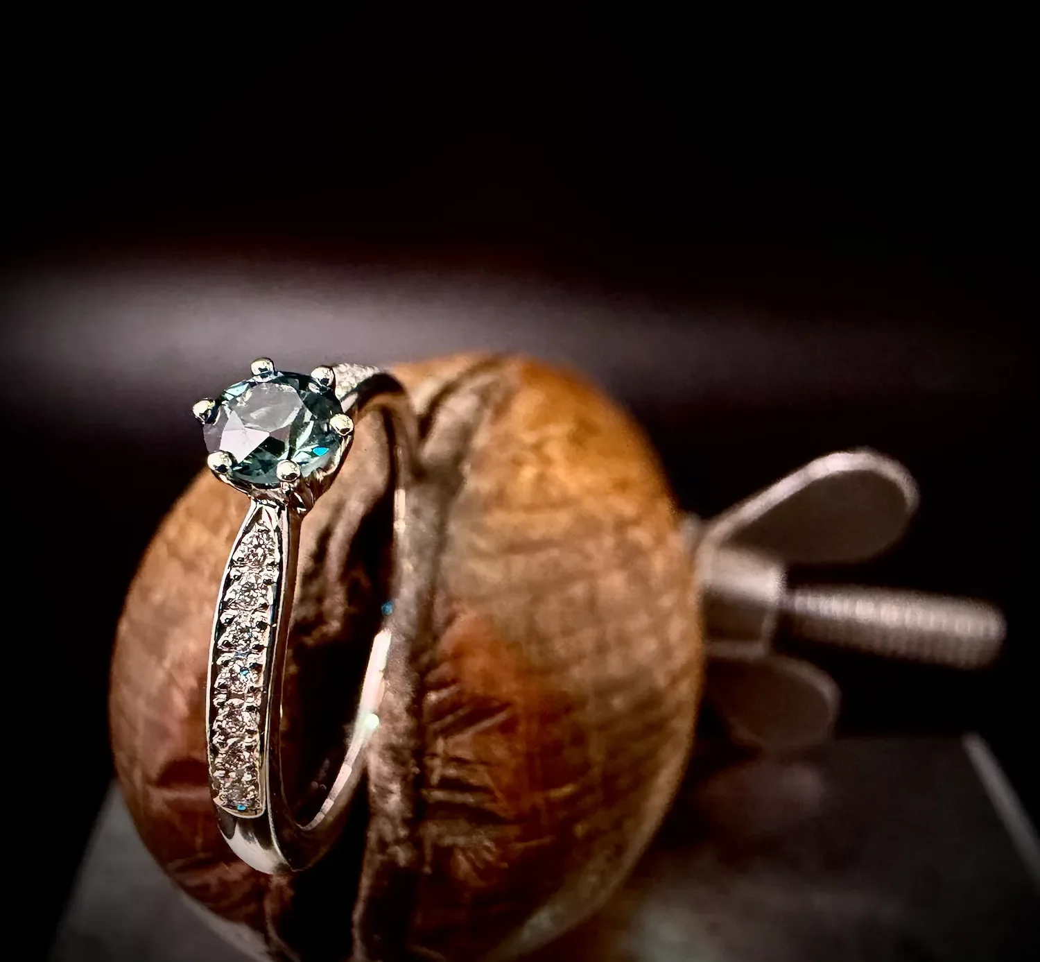 Weißgold-Verlobungsring mit Teal-Saphir und Diamantschiene auf Holzmodell, Isarschmiede München.